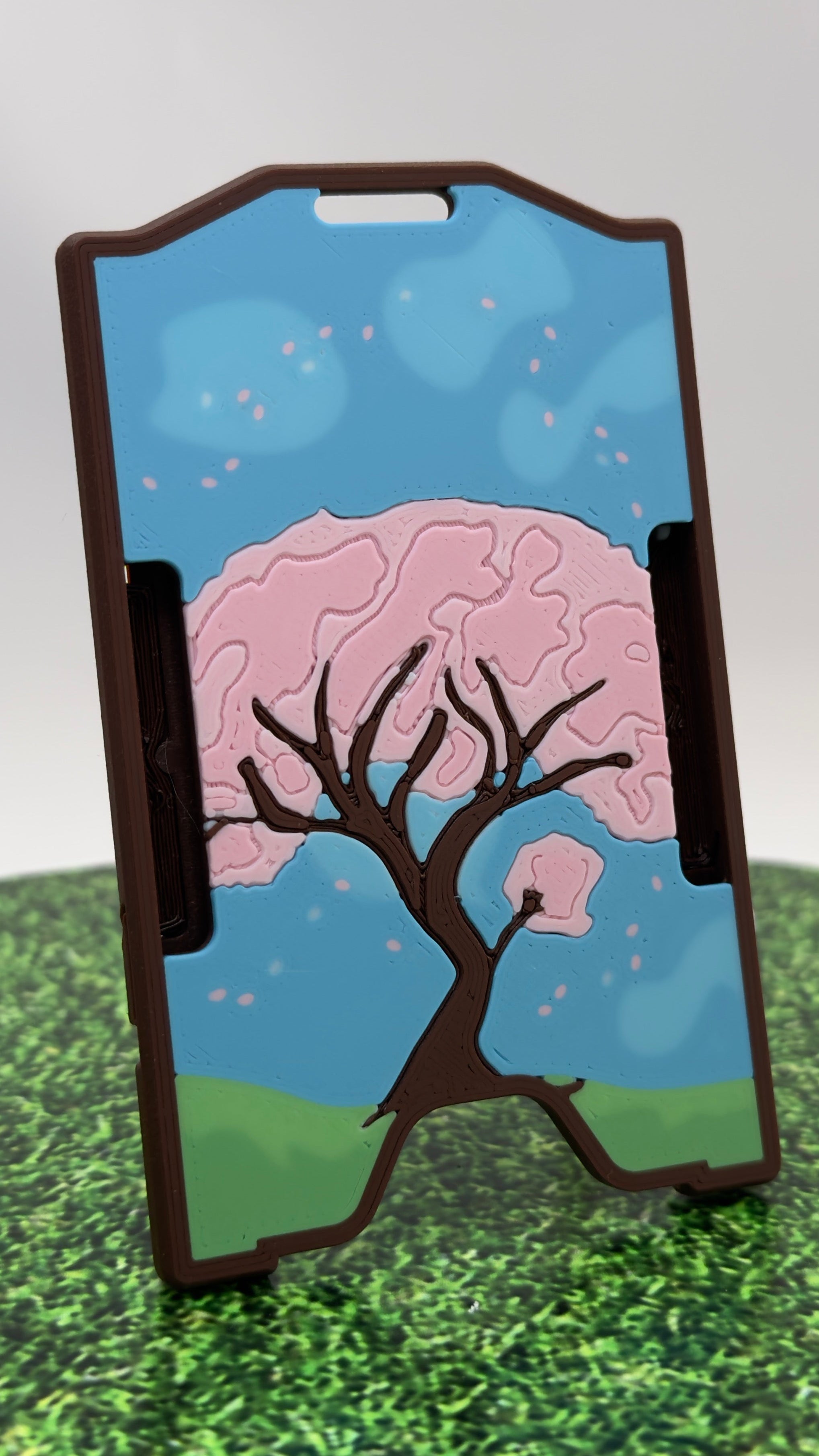 A keycard holder with a printed cherry blossom tree design, standing on a pink and white surface against a light gray background.